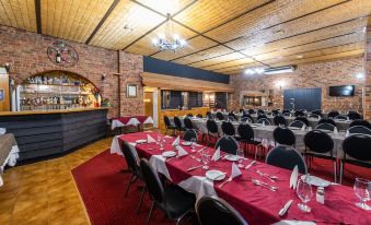 a large dining room with multiple tables covered in red tablecloths , set for a formal dinner at Golden Age Motor Inn