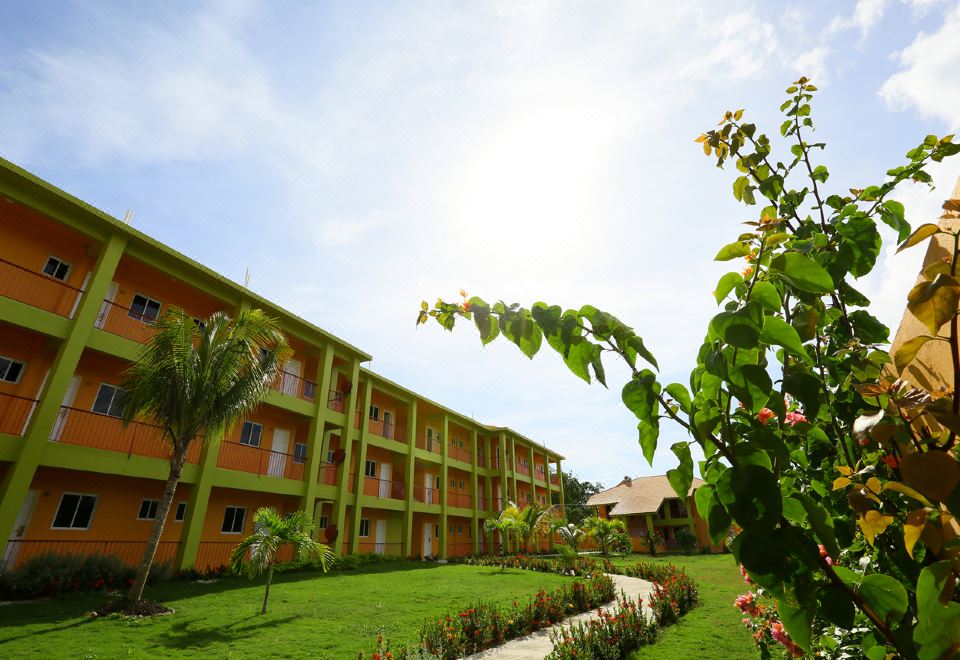a resort with multiple buildings , green grass , and trees , under a clear blue sky with sunlight shining through at Oasis Resort