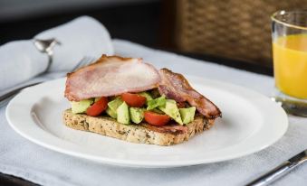 a plate of food , consisting of a sandwich with bacon and avocado , is placed on a table at Peartree Hill