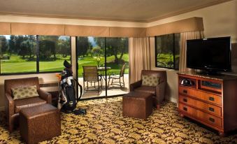 a well - furnished living room with a couch , chairs , and television in front of a large window overlooking a golf course at Singing Hills Golf Resort