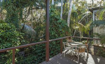a wooden deck surrounded by lush greenery , with a dining table and chairs on the deck at Discovery Parks - Emerald Beach