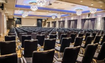 an empty conference room with rows of black chairs and chandeliers , set against a backdrop of a large screen at Hotel Alexandra Loen