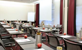a conference room with rows of tables and chairs , each table has a red apple placed on it at Mercure Villeneuve Loubet Plage