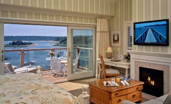 a bedroom with a bed , fireplace , and television is shown with a view of the water through the window at Wequassett Resort and Golf Club