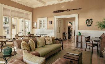 a spacious living room with beige walls , a green couch , and a wooden surfboard hanging on the wall at Rosewood Kauri Cliffs