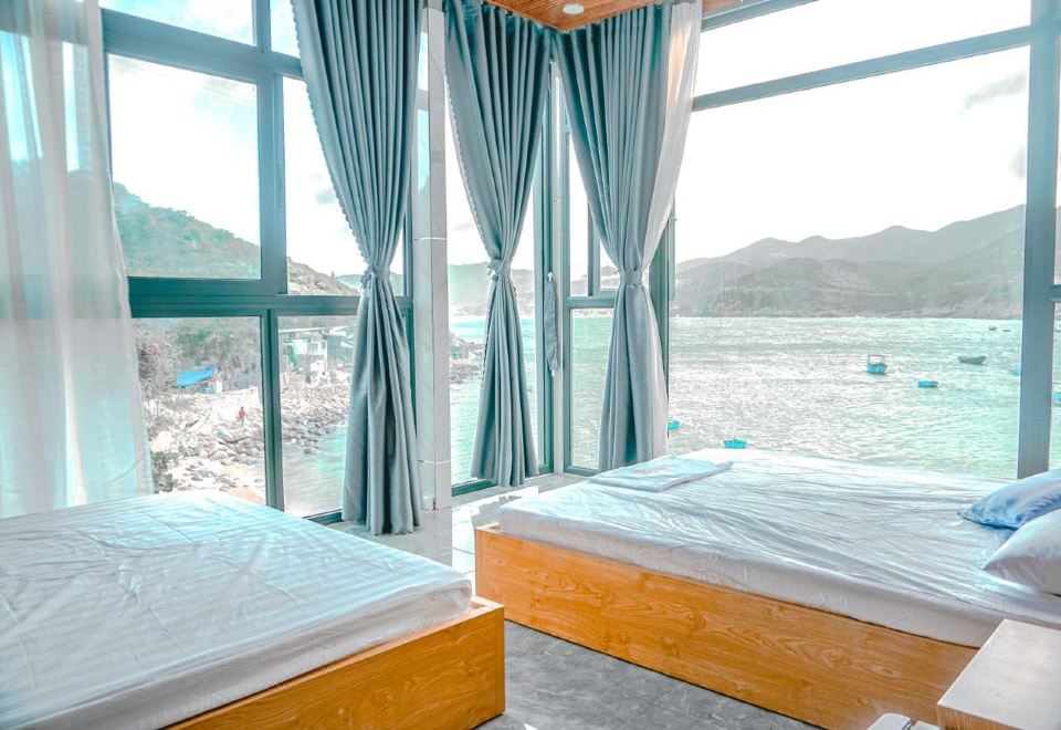 a room with two beds and large windows overlooking a body of water , creating a serene atmosphere at The Sea Rock Binh Hung