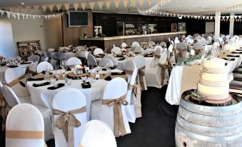 a wedding reception with multiple tables set for guests , each with white tablecloths and chairs adorned with gold ribbons at Marsden Lake Resort Central Otago