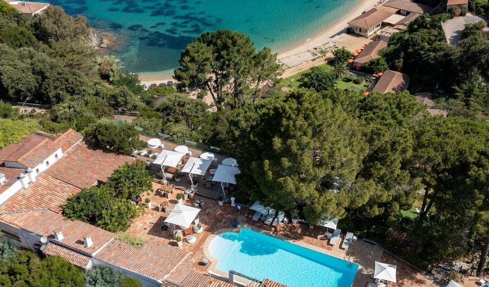 a resort with a large pool surrounded by lounge chairs and umbrellas , as well as a beach nearby at A’mare Corsica Seaside Small Resort