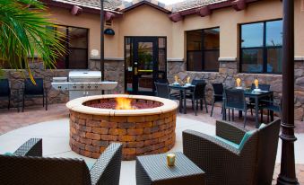 a brick patio with a fire pit surrounded by tables and chairs , providing a cozy atmosphere for outdoor dining at Sonesta ES Suites Phoenix Goodyear