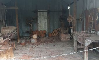 an old building with a brick floor , wooden furniture , and various tools displayed in the room at Deniliquin Pioneer Tourist Park