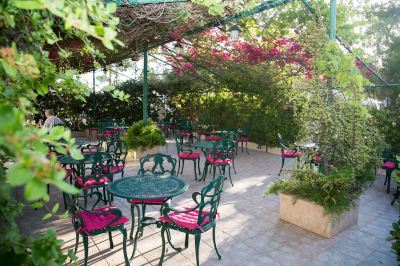 an outdoor dining area with green tables and chairs under a canopy of pink flowers at Hotel Summery