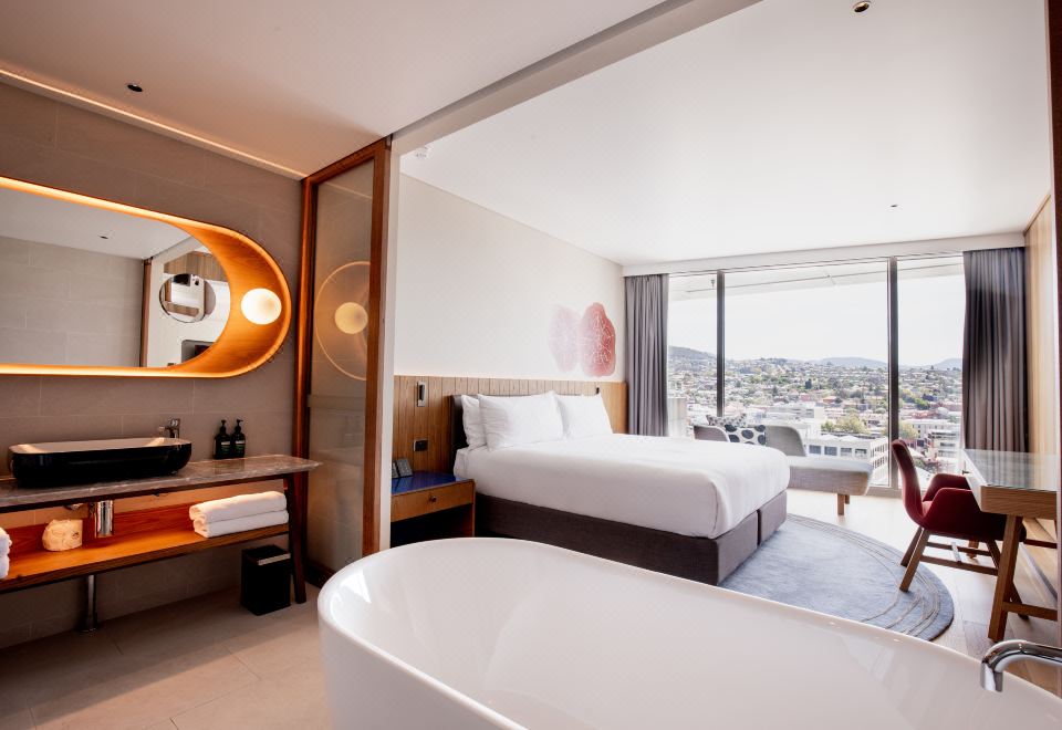 a hotel room with a bed , bathtub , and large window , providing a view of the city at Crowne Plaza Hobart, an IHG Hotel