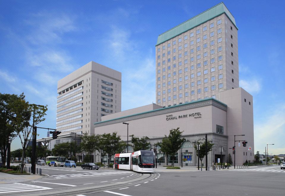 a large hotel building with a bus stop in front , located on a busy city street at Oarks Canal Park Hotel Toyama