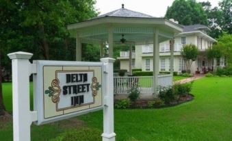 "a sign for the "" delta street inn "" is displayed in front of a building with a white picket fence" at Delta Street Inn