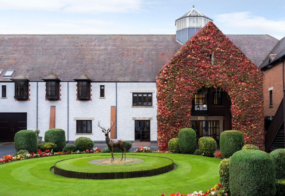 a red brick building with ivy - covered walls and a large white building , as well as a statue of a deer in the middle of a at Forest of Arden Country Club