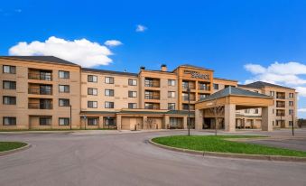 a large , modern hotel building with multiple floors , surrounded by green grass and trees , under a clear blue sky at Sonesta Select Detroit Novi