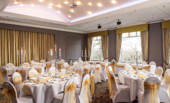 a beautifully decorated banquet hall with multiple tables set for a formal event , including white tablecloths , gold chairs , and multiple candlesticks at Mercure Bradford Bankfield Hotel