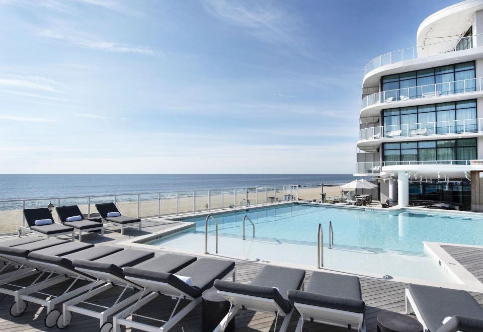 a swimming pool and sun loungers on a deck with ocean in the background , under a clear blue sky at Wave Resort