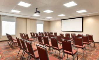 a large conference room with rows of red chairs arranged in a semicircle , and a projector mounted on the wall at Home2 Suites by Hilton Milwaukee Brookfield