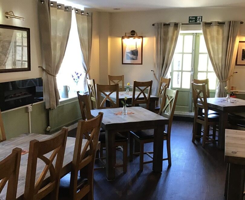 a well - decorated dining room with wooden tables and chairs , along with a fireplace in the background at Crossways Inn