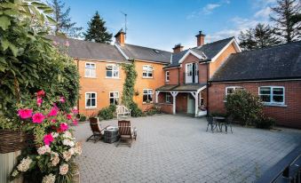 a brick house surrounded by a paved courtyard , with several chairs and benches placed around it at Lisnacurran