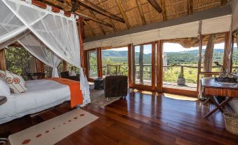 a spacious bedroom with wooden floors , large windows , and a view of the outdoors through the balcony at Pumba Private Game Reserve