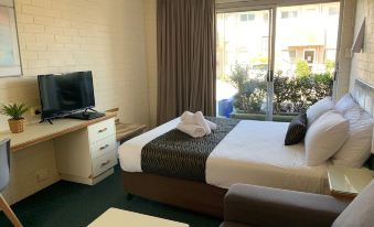 a bedroom with a bed , television , and couch near a sliding glass door leading to a patio at Crest Motor Inn