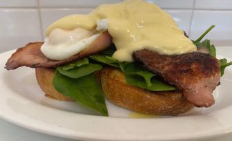 a white plate with a sandwich topped with spinach and bacon , topped with a hollandaise sauce at Parry Creek Farm Tourist Resort & Caravan Park