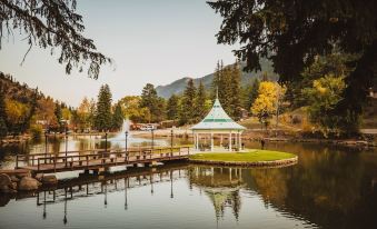 a serene lake with a gazebo and a wooden walkway , surrounded by lush greenery and mountains in the background at Little Beaver Inn