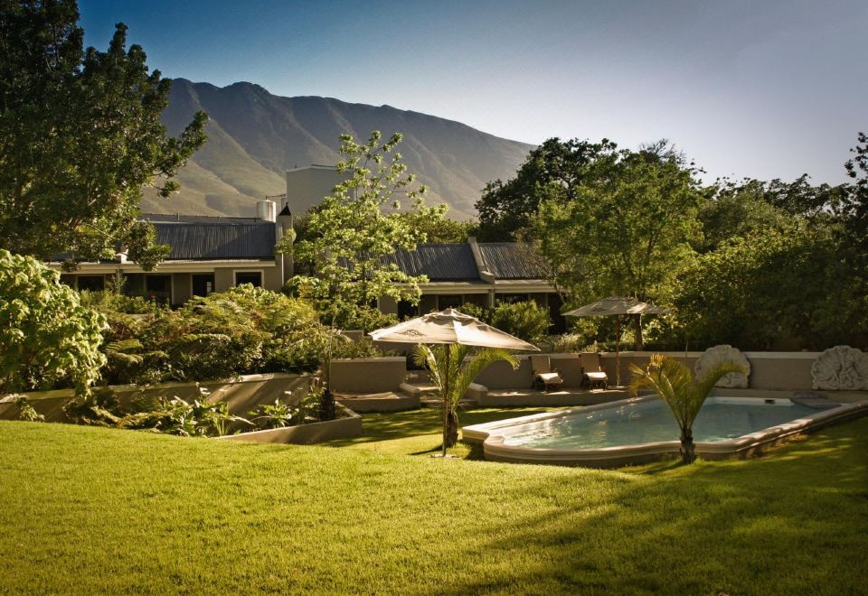 a serene backyard with a pool surrounded by lush green grass and trees , overlooking a mountainous landscape at Schoone Oordt Country House