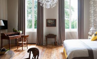 a spacious bedroom with hardwood floors , two windows , and a chandelier hanging from the ceiling at Les Sources de Cheverny