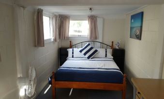 a small bedroom with a wooden bed , blue and white bedding , and a window with curtains at Sailors Rest
