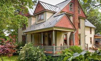 a large , two - story house with a red roof and white trim is surrounded by greenery at Gothic Eves Inn and Spa Bed and Breakfast