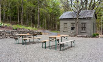 a wooden bench and table set up in a gravel area near a house , surrounded by trees at Stonehill's Farmhouse