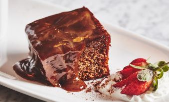 a white plate with a slice of chocolate cake , topped with whipped cream and strawberries , placed on a dining table at The Garrison