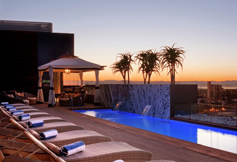 a rooftop pool with lounge chairs and palm trees , overlooking the ocean at sunset at Hilton Windhoek