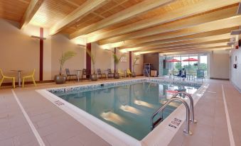 an indoor swimming pool with a wooden ceiling , surrounded by lounge chairs and umbrellas , in a well - lit room at Home2 Suites by Hilton Hagerstown