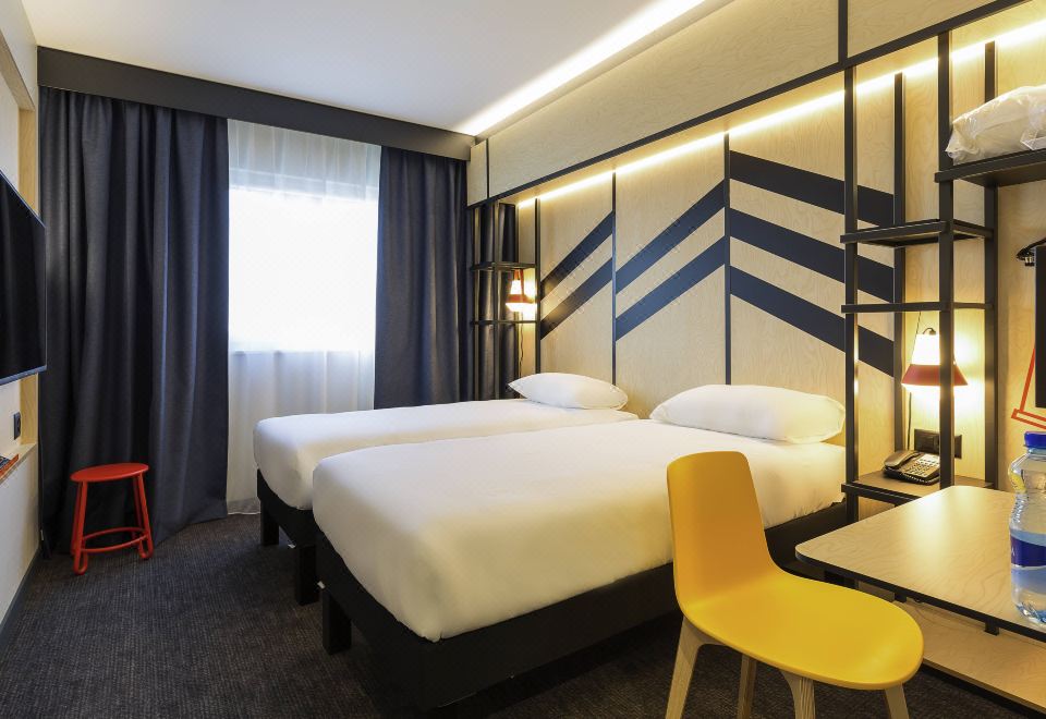 a modern hotel room with two beds , a desk , and a window , decorated in black and white geometric patterns at Ibis Styles Genève Palexpo Aéroport