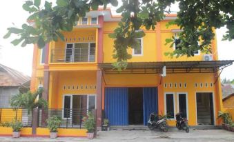 a yellow house with blue doors and windows , surrounded by trees and parked motorcycles in front at Sinar Harapan