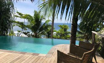 a wooden deck with palm trees and a swimming pool , overlooking the ocean , from a high vantage point at Moro Ma Doto