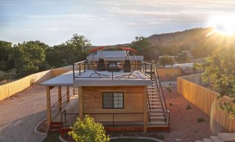 a wooden house with a balcony and red chairs is surrounded by trees and hills at The Escape to East Zion