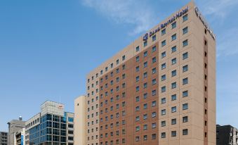 "a large building with a blue sign on top and the words "" dubai bourseage hotel "" below it" at Daiwa Roynet Hotel Oita