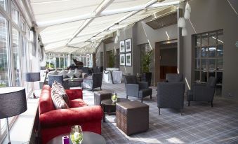 a modern lounge area with various seating arrangements , including couches and chairs , under a large ceiling at Village Hotel Chester St David's