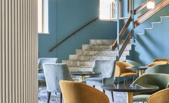 a modern office space with blue walls , a staircase leading to the second floor , and various tables and chairs arranged for work or business at Hotel Astoria