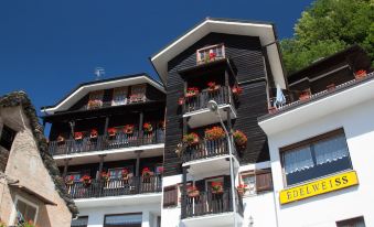 a three - story building with a black and white color scheme , featuring flower arrangements on the balconies at Hotel Edelweiss