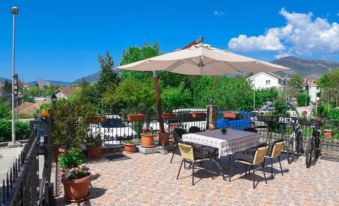 a patio with a table and chairs , an umbrella , potted plants , and a pool in the background at D&D Apartments