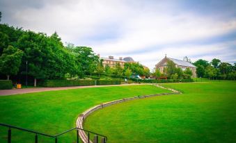 a grassy field with a curved path and a building in the background , under a cloudy sky at Station House Hotel Letterkenny