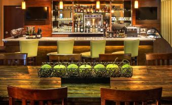 a well - stocked bar with various bottles and glasses , as well as several chairs and tables surrounding it at DoubleTree by Hilton Portland - Tigard