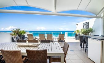 a rooftop patio with a dining table and chairs set up for a meal , overlooking the ocean at Rolling Surf Resort Sunshine Coast