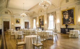 a large , elegant room with white tablecloths and gold chairs is decorated with paintings and chandeliers at Oheka Castle Hotel & Estate